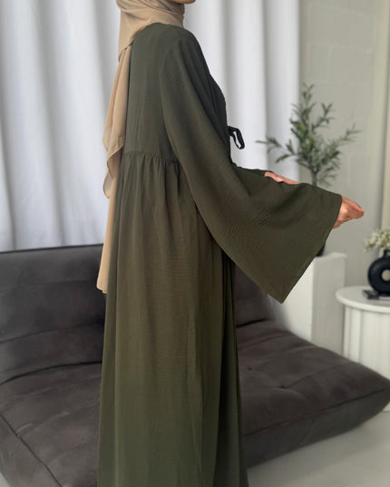 Woman wearing a long olive green dress with a beige hijab in a room.
