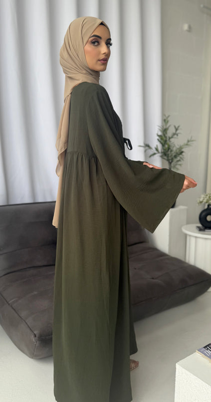 Woman wearing a long olive green dress with a beige hijab in a room.