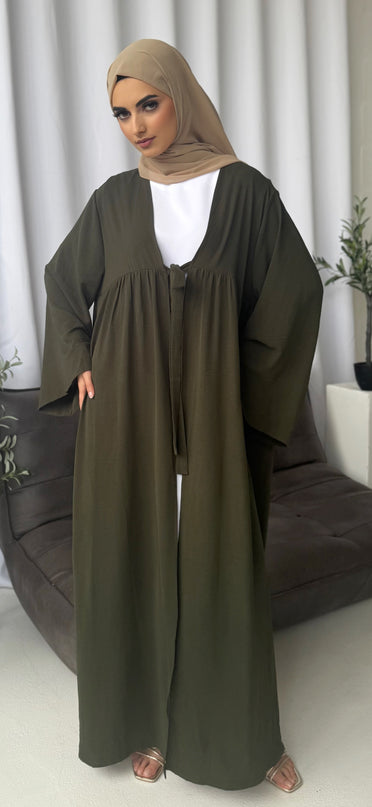 Woman wearing an olive green abaya with a white top, standing against a neutral background.